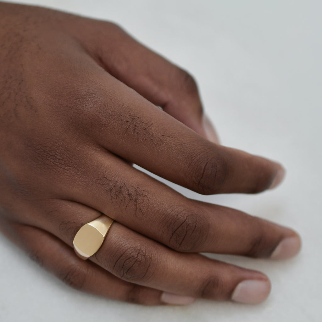A square 9K gold signet ring worn on a man’s finger.