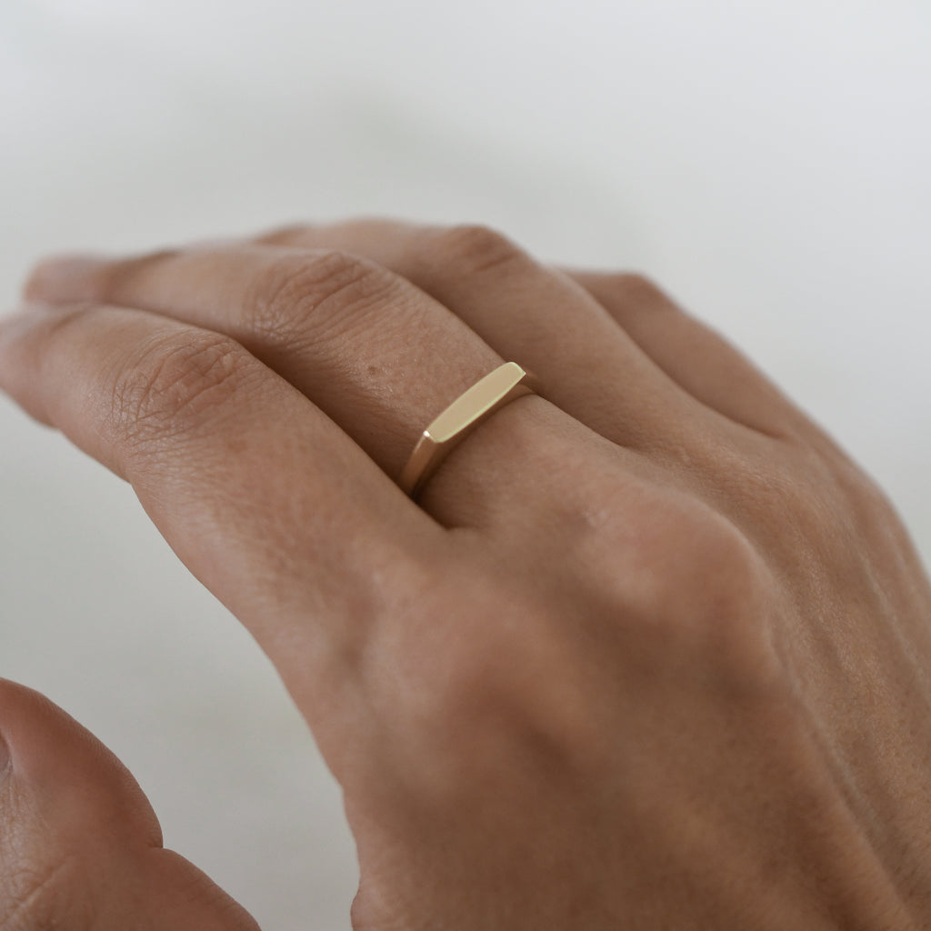 A rectangular 9K gold signet ring shown on a woman’s hand.