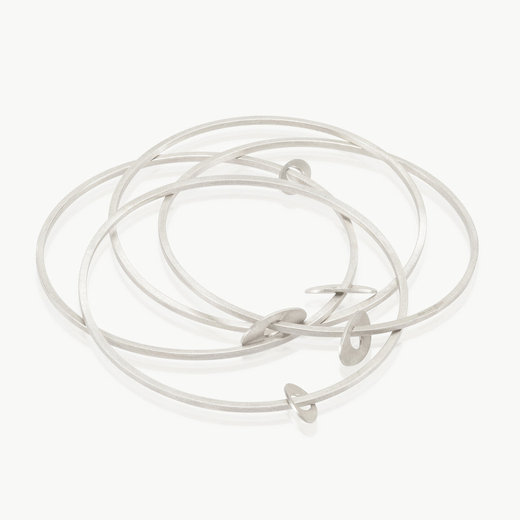 An interconnected set of 4 narrow sterling silver bangles with free-hanging oval charms. Made in Cape Town with high-quality craftsmanship for 15 years.