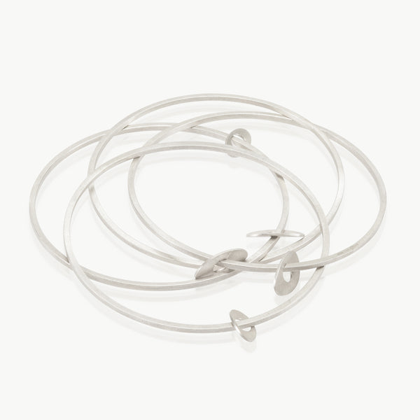 An interconnected set of 4 narrow sterling silver bangles with free-hanging oval charms. Made in Cape Town with high-quality craftsmanship for 15 years.