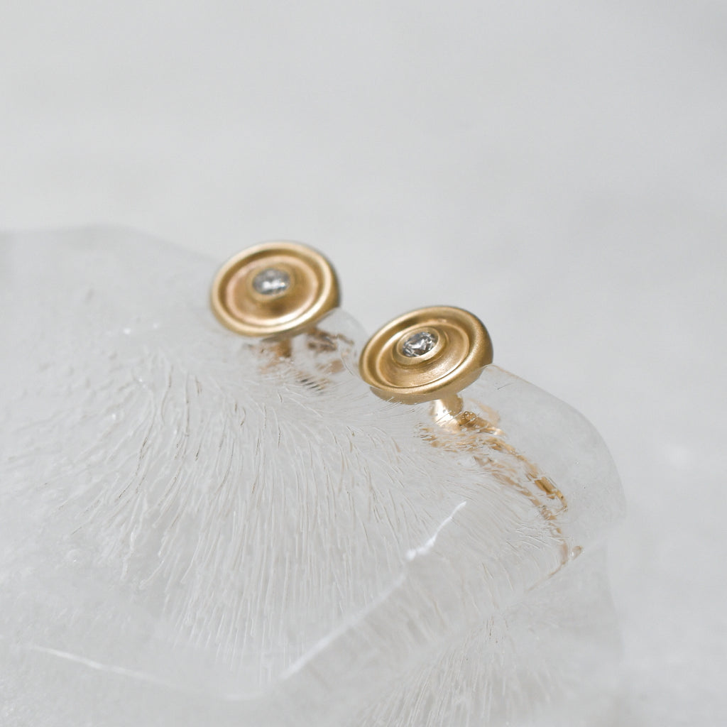 Gold earrings with a central lab-grown diamond on a block of ice.