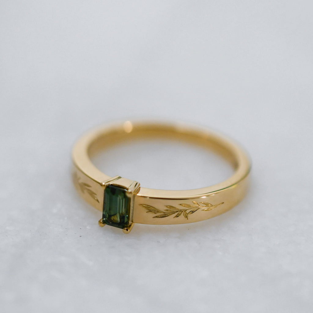 Ethical jewellery piece with a four-prong green sapphire and leaf-engraved gold band