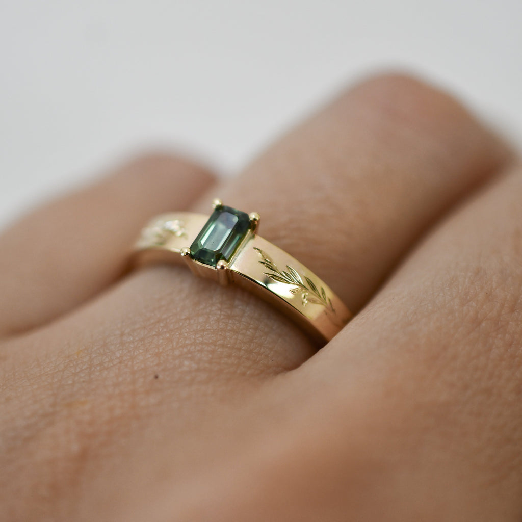 Handmade green sapphire ring worn on a woman's hand, set in 9ct gold with engraved leaf detail