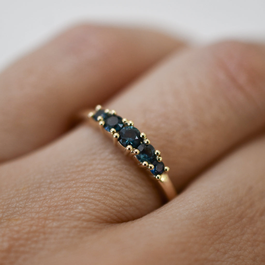 Woman's hand wearing a handmade gold ring set with five graduated blue sapphires