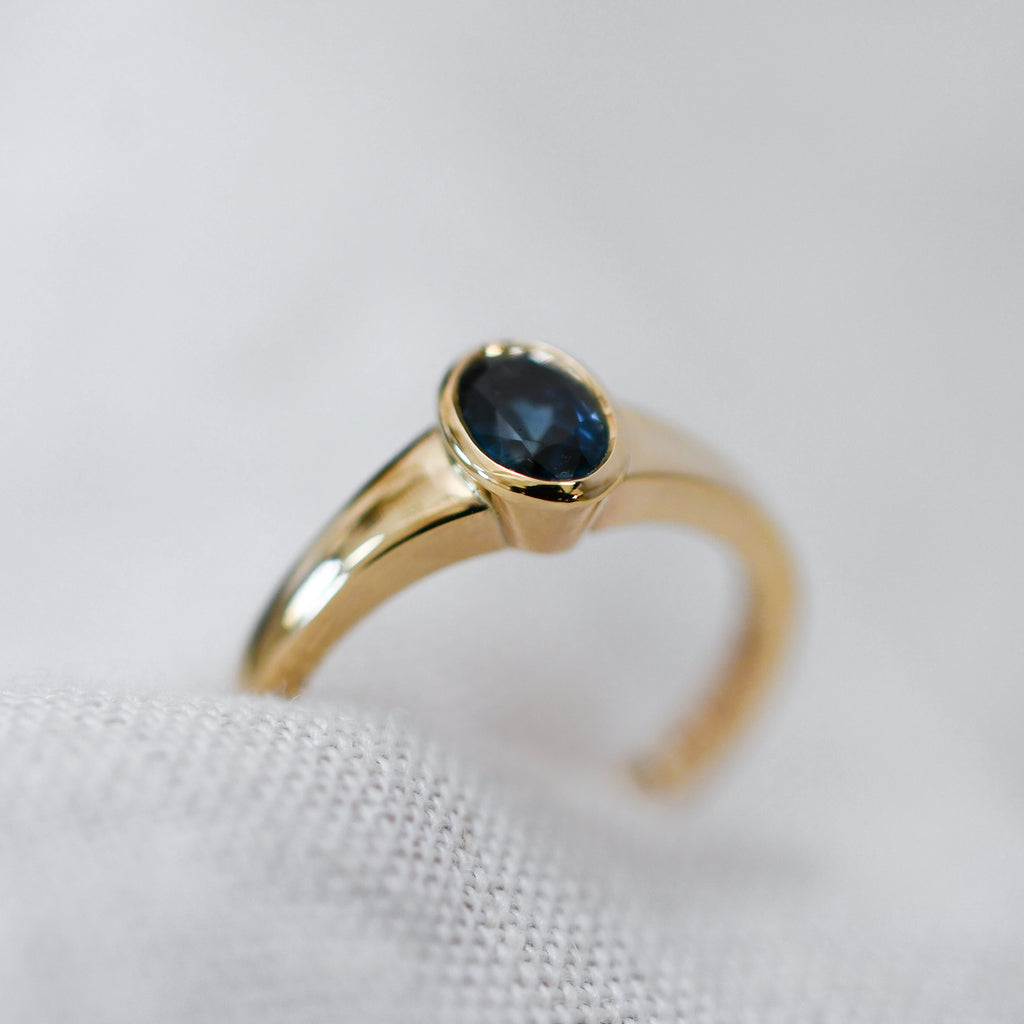 Close-up of an oval blue sapphire in a polished gold bezel setting