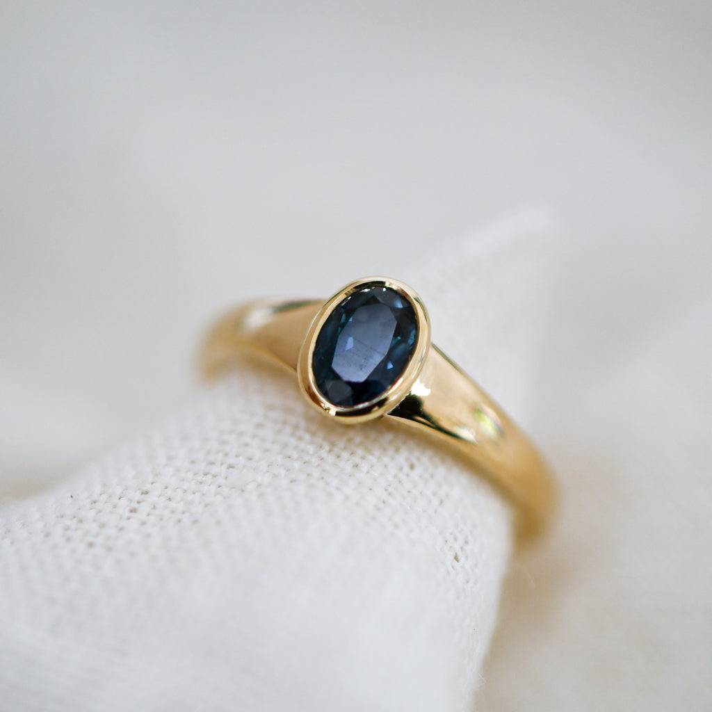 Ethically sourced blue sapphire in a polished gold bezel setting, close-up