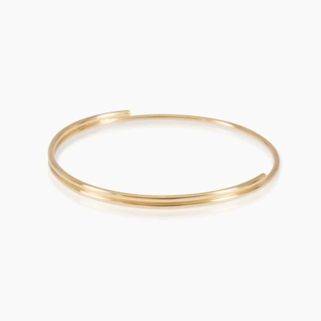 Flow bangle crafted in 9k yellow Fairmined gold with soft organic curves. Minimalist gold jewellery inspired by the movement of water.