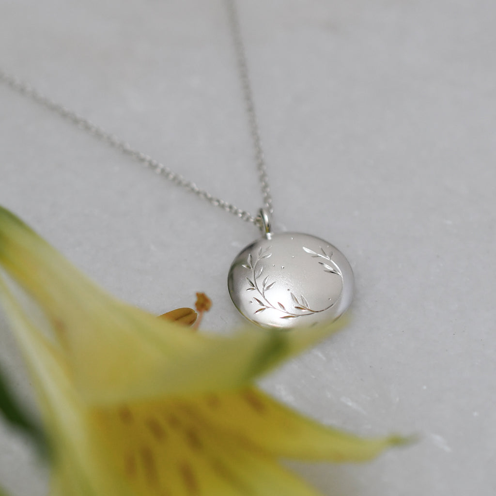 Ethical sterling silver round pendant with soft matte-polished finish and hand-engraved botanical design.
